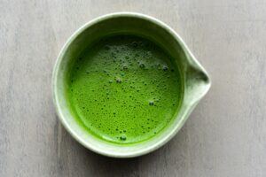 A bowl of vibrant green matcha tea in a white ceramic cup, viewed from above