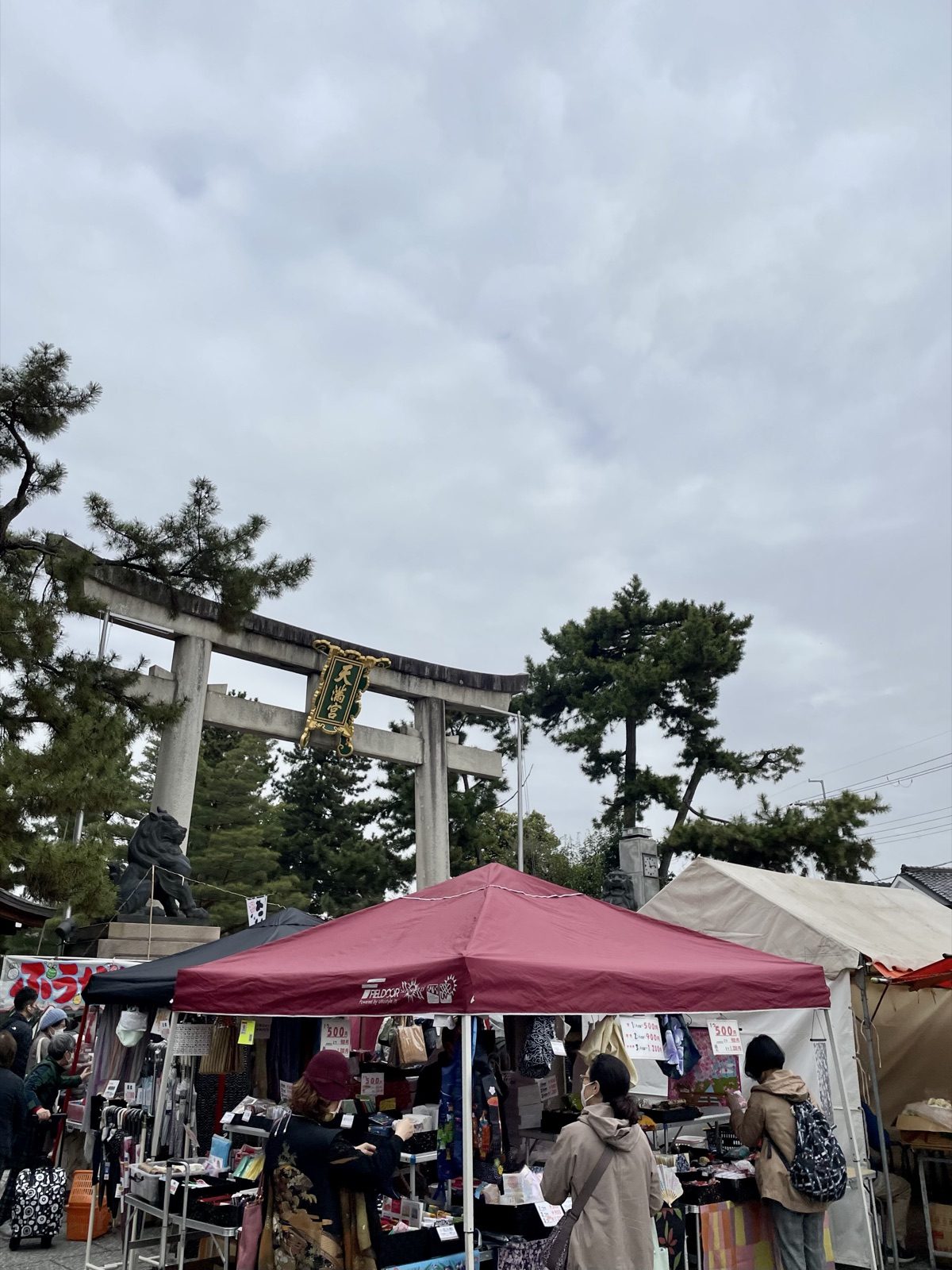 Market stalls in front of the stone torii at Kitano Tenmangu during the Tenjin-san flea market