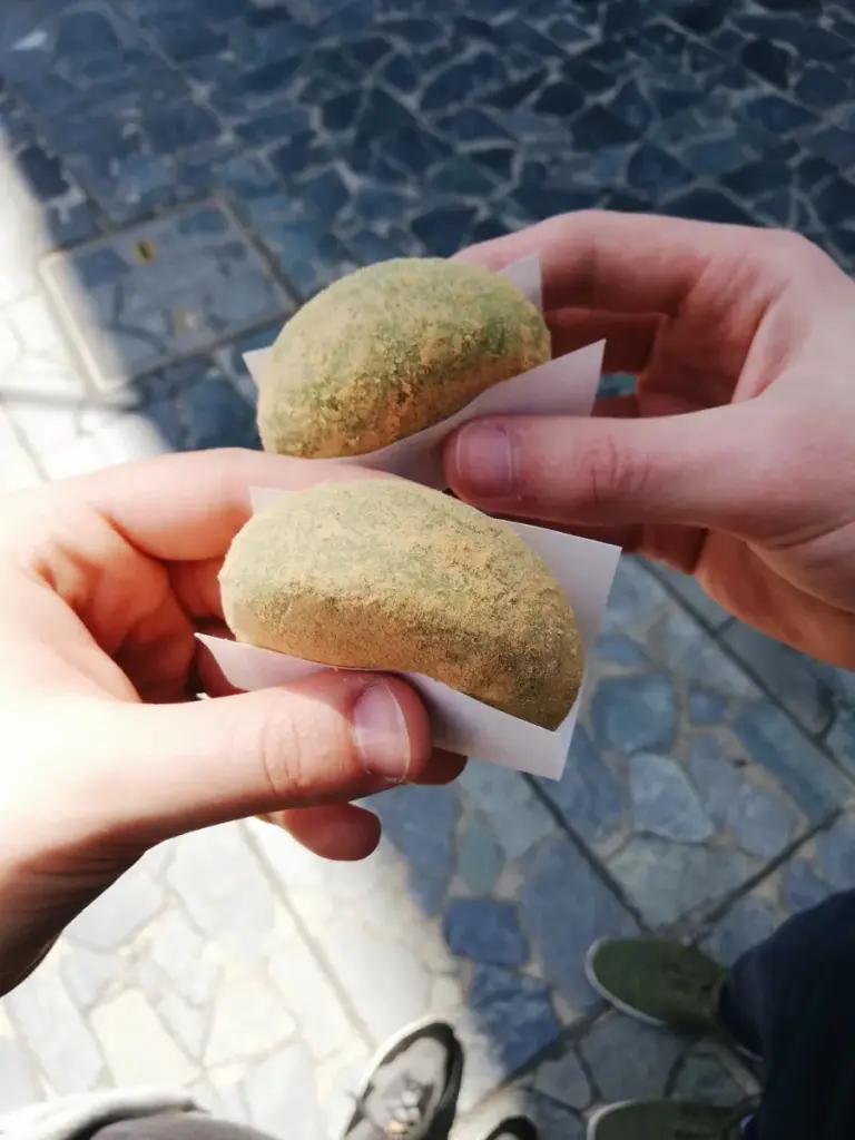 Two hands holding green mochi dusted with kinako