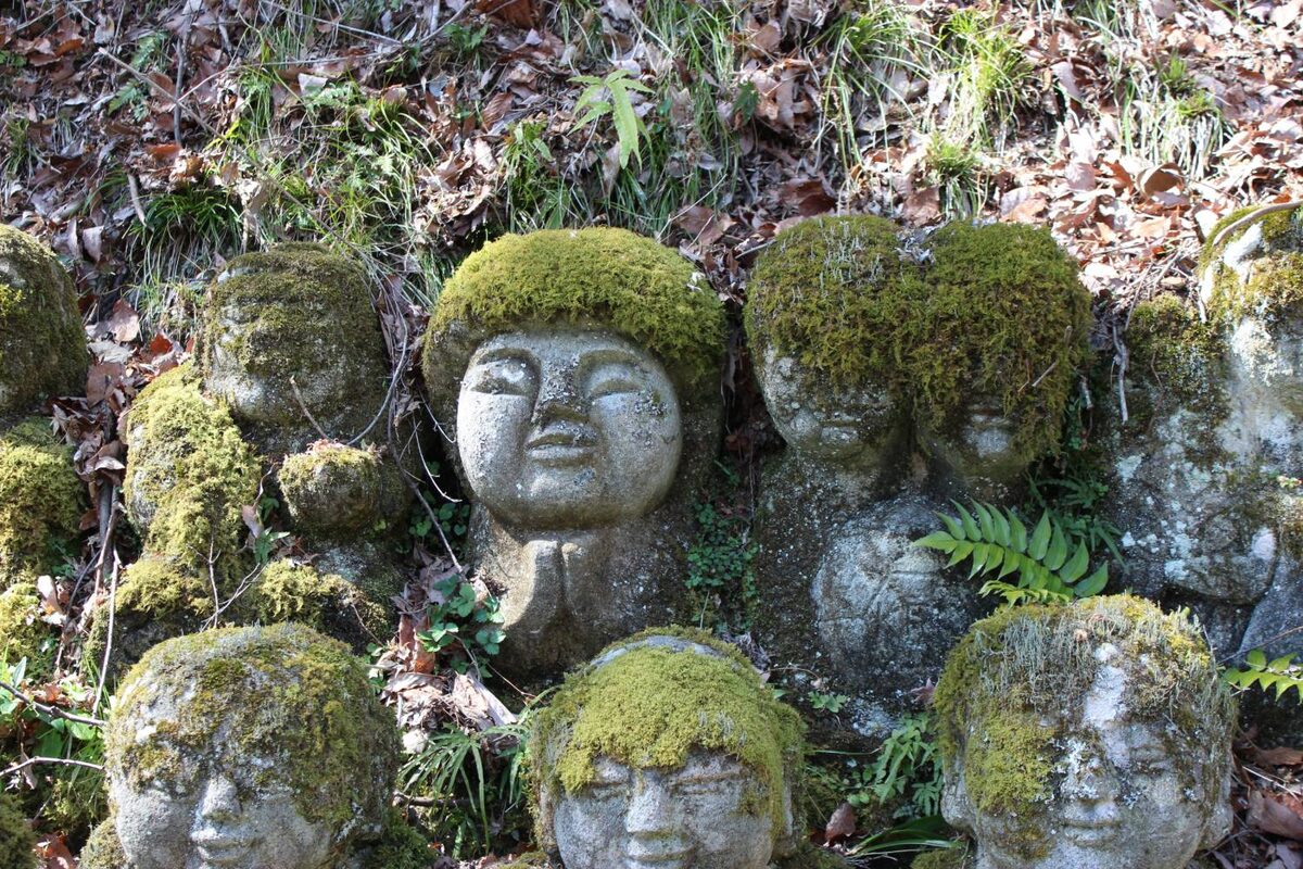 Small stone statue with moss hair between fallen leaves at Otagi Nenbutsu-ji